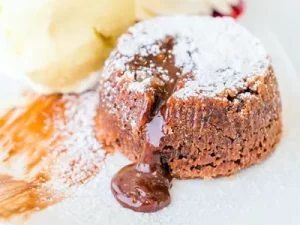 Čokoladna sladica, souffle, posuta s sladkorjem v prahu, iz katere teče čokolada in je postrežena z vanilijevim sladoledom na belem krožniku